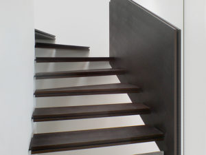 Holztreppe. Treppe Eine in der Wand überputzte Metallwange hält ein System aus mehrschichtigen Stufen.